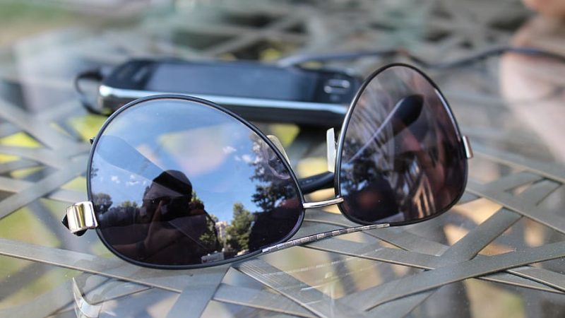 Close-up of sunglasses placed on a table with a smartphone in the background